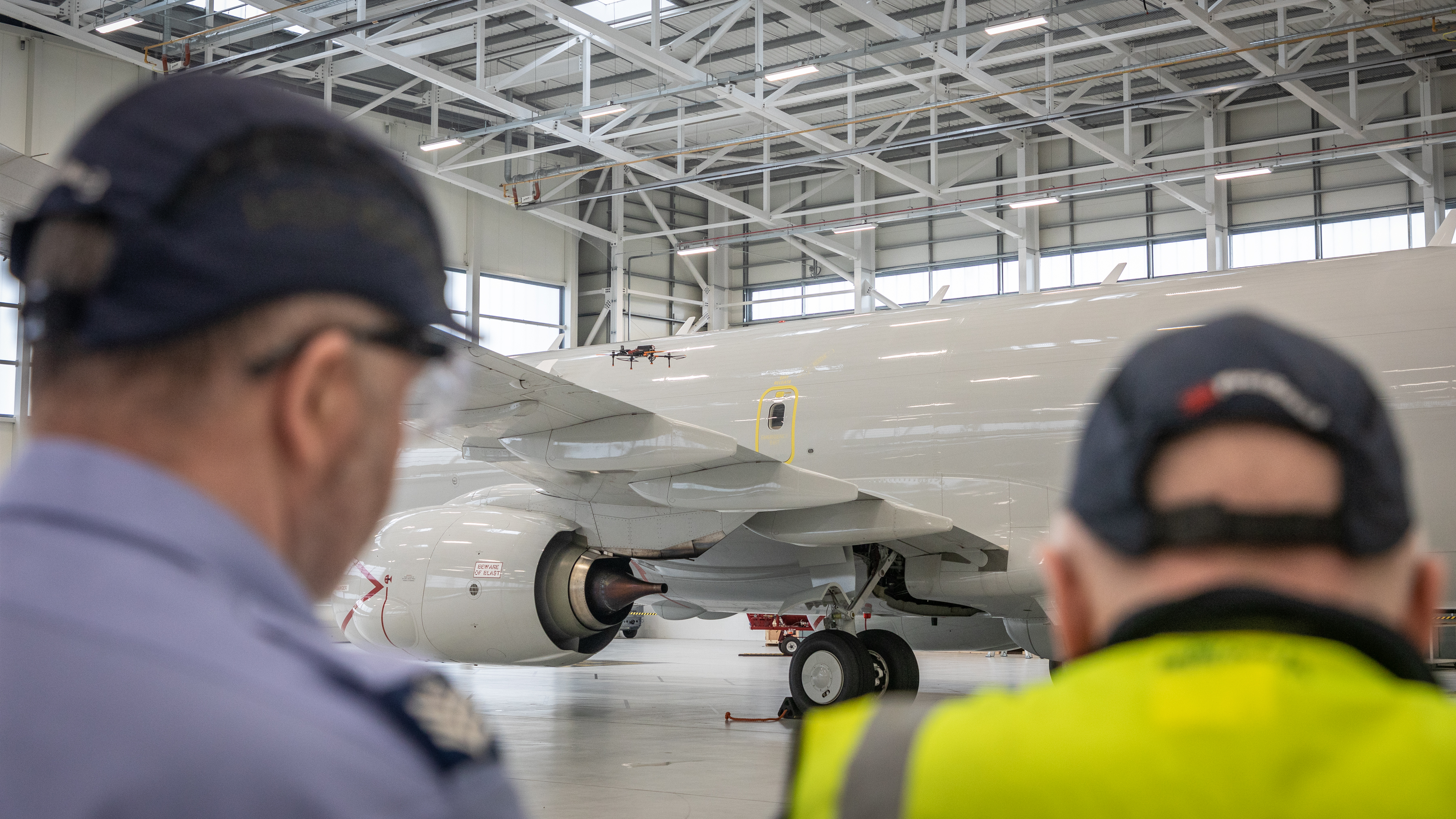 Engineers standing in front of an aircraft in a hangar as a drone flies alongside it